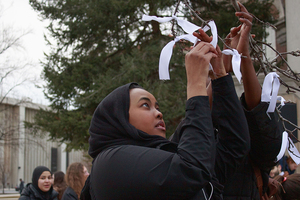 Saadiya Sheekh-Nuur, a senior at SUNY-ESF, ties a ribbon to a tree outside Hendricks Chapel as an act of remembrance for the 50 victims of the shootings. 