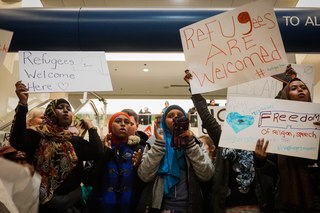 Former refugees and Syracuse residents hold signs and chant, 