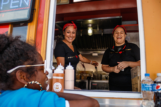 As her food is being prepared by owner Lisa Greene (center) and worker Casey Greene (right), Tamiko Smith (left) proclaims herself the number one customer of Poutine Gourmet’s food stand.